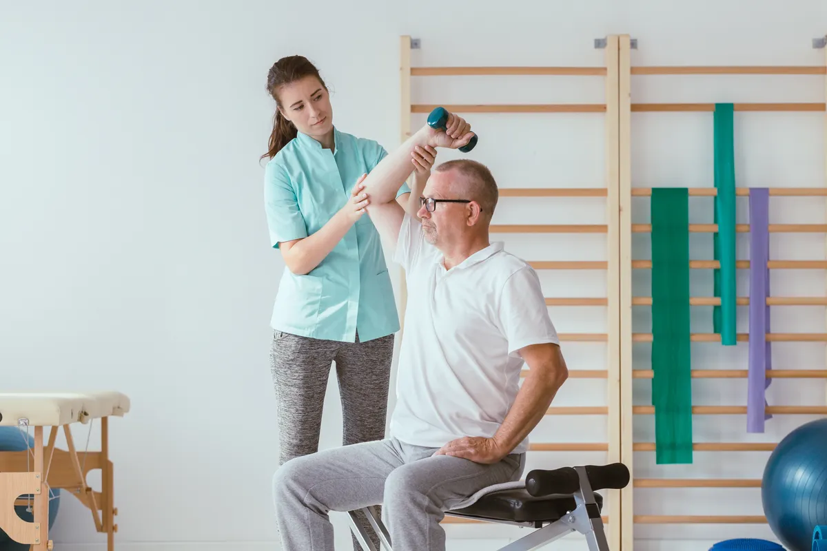 Physiotherapist assisting a senior patient performing weight exercises